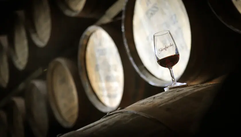 Kieliszek whisky Glenfarclas na beczce, symbol najlepszych technik leżakowania whisky finiszowanie w beczkach po sherry.