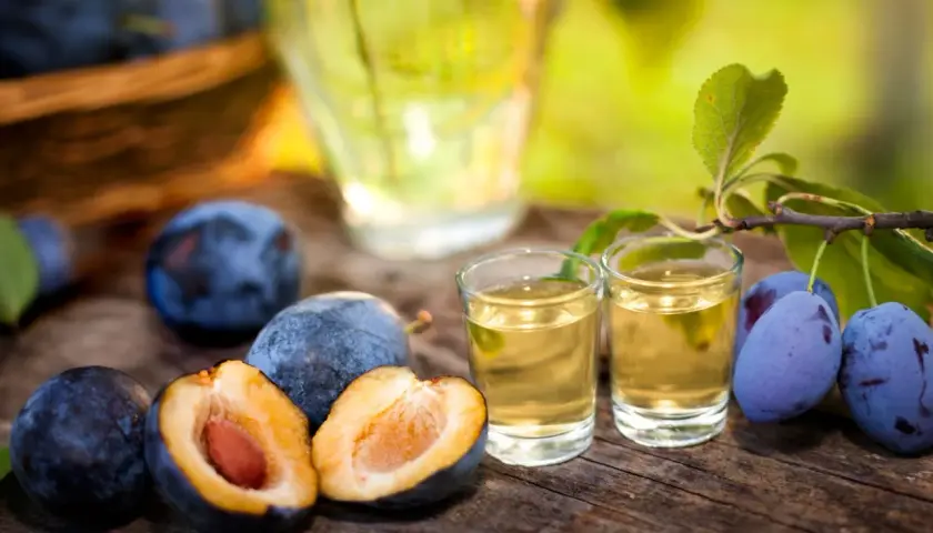 Jak przygotować domową nalewkę na whisky z suszonymi śliwkami? Dojrzałe śliwki i dwa kieliszki złocistego trunku na drewnianym stole.