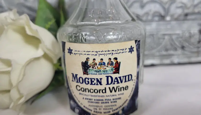 Butelka wina Mogen David Concord Wine z etykietą i białym kwiatem w tle.