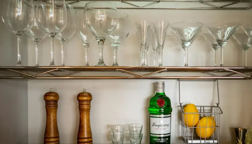 Czy bittersy (np. angostura) są niezbędne w domowym barku? Na półce stoją kieliszki, gin, cytryny i młynki do przypraw.