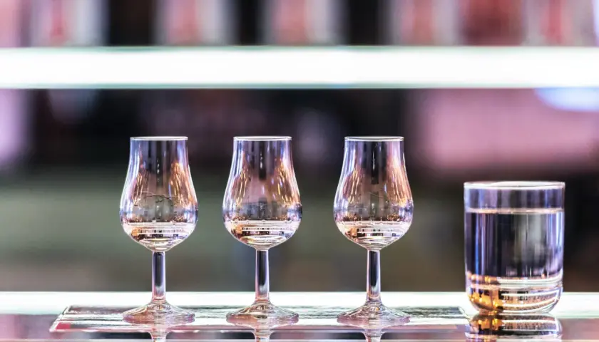 Degustacja wódek gatunkowych krok po kroku: trzy kieliszki degustacyjne i jeden szklany kieliszek z wodą.