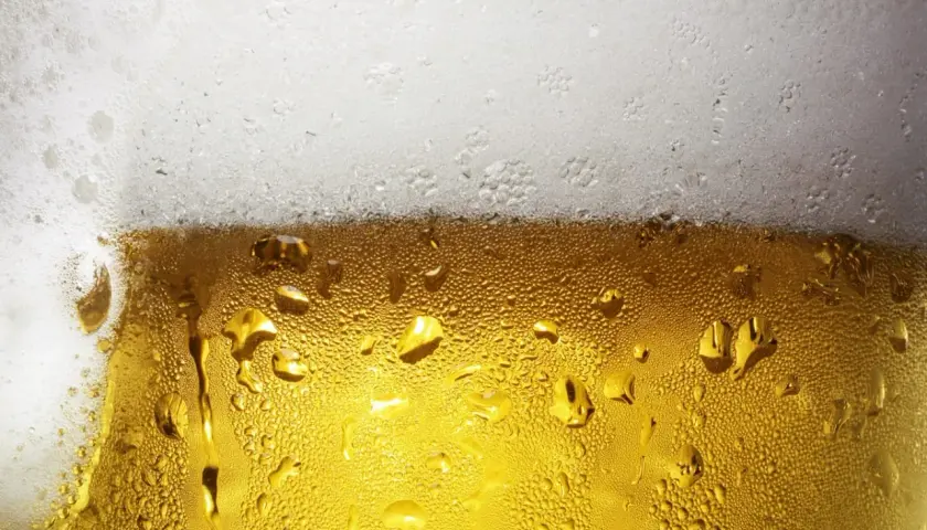 Zbliżenie na szklankę piwa z kroplami kondensacji i białą pianką na górze.