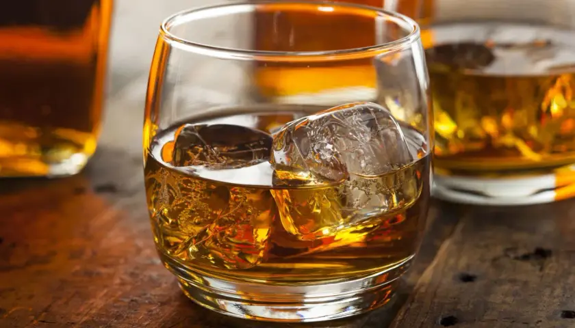 Szklanka whisky z lodem na drewnianym stole. Dowiedz się o różnicy między whisky szkocką a kanadyjską i irlandzką wymogi prawne.