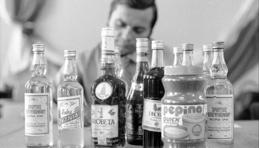 Mężczyzna bada butelki z alkoholem, w tym wódkę i brandy. Proces kupażowania może prowadzić do mętnienia wódki po dodaniu wody.