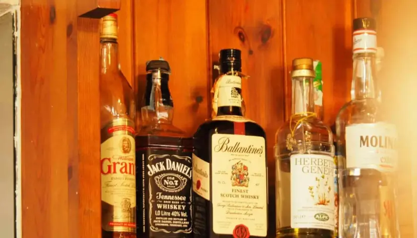 Butelki whisky na drewnianej półce. Zwróć uwagę na zmętnienie i osad w starych butelkach, by rozpoznać objawy zepsutej whisky.