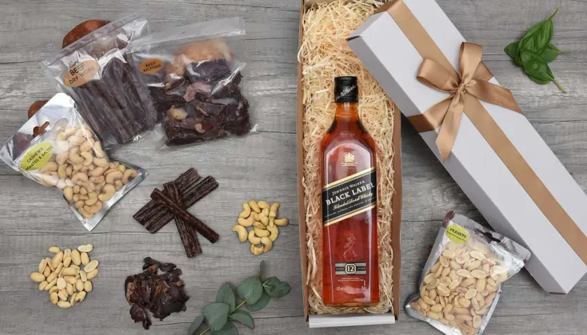 Jak przygotować prezentowy zestaw whisky dla początkującego konesera: butelka Johnnie Walker Black Label, suszone mięso, orzechy i eleganckie pudełko.