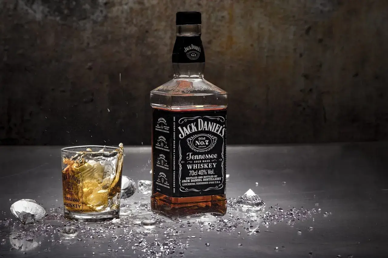 Butelka i szklanka Jack Daniel's na metalowym blacie, z lodem i błyszczącymi drobinkami. Czy whisky jest zdrowe? To pytanie pozostaje otwarte.