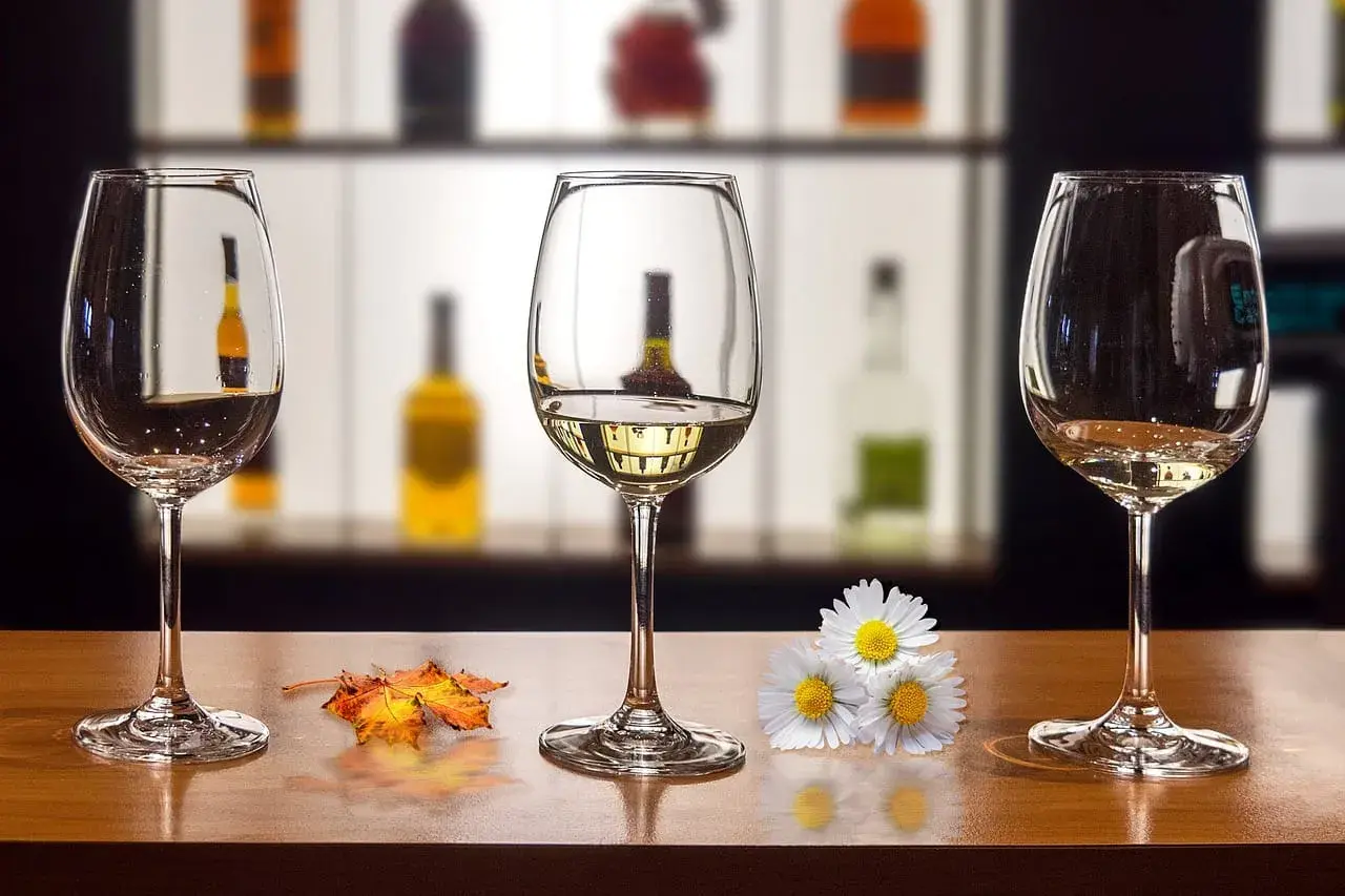 Trzy kieliszki na drewnianym blacie. Jak usunąć zapach alkoholu z kieliszka przed ponowną degustacją? Jesienne liście i kwiaty dodają uroku.