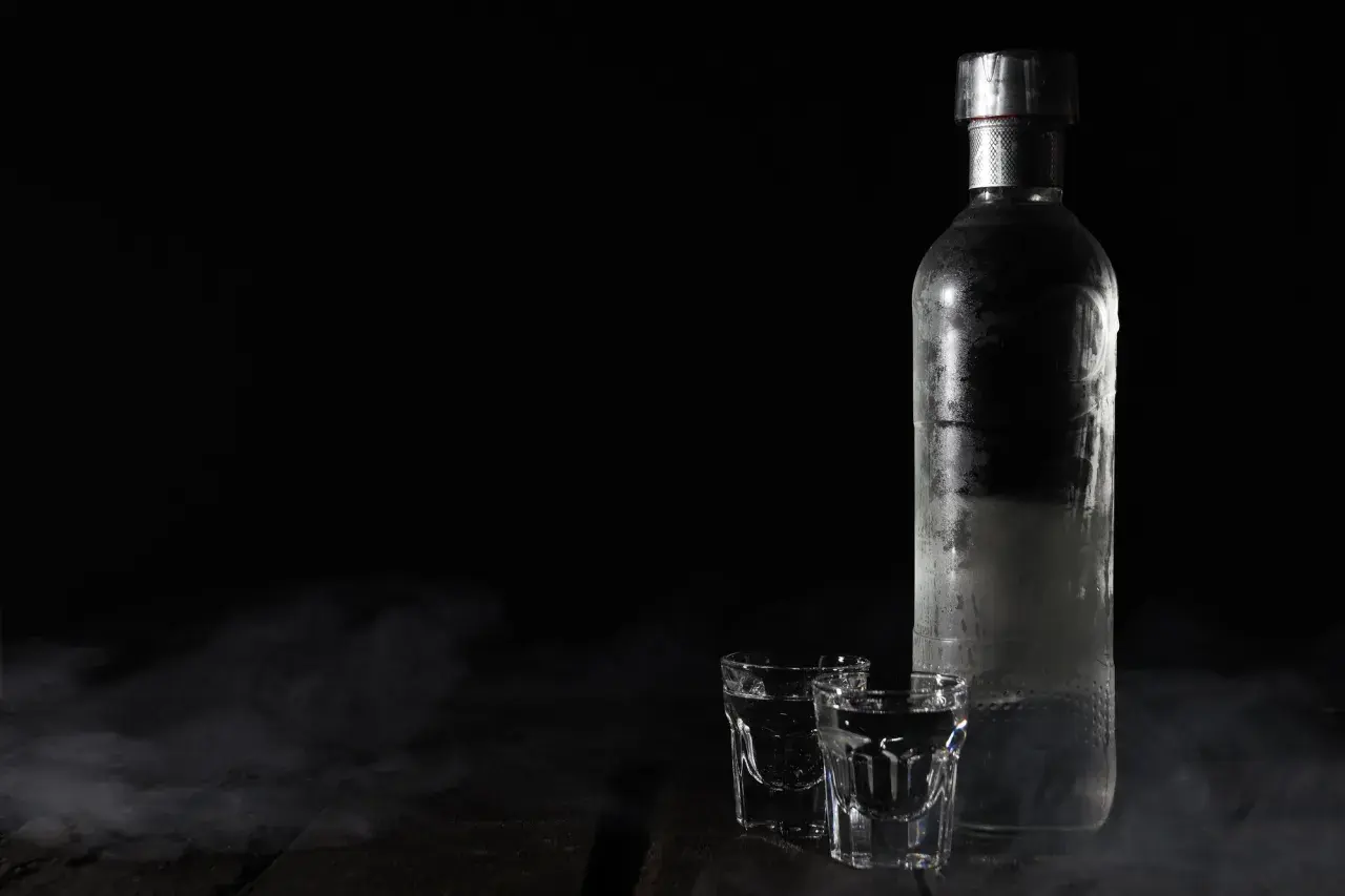 Chłodna wódka w butelce i kieliszkach, otoczona mgiełką. Czy otwarta wódka traci procenty? Tajemnica nocy.