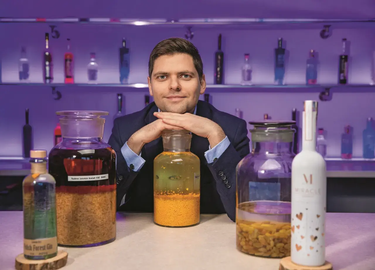 Ekspert prezentuje najlepsze techniki produkcji wódek rzemieślniczych (craft vodka), otoczony butelkami i słoikami z nalewami.