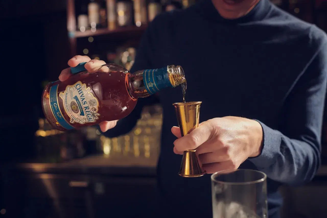 Mężczyzna nalewa whisky Chivas Regal do miarki. Czy whisky podnosi cukier? To pytanie zadaje sobie wielu, ale alkohol sam w sobie nie zawiera cukru.