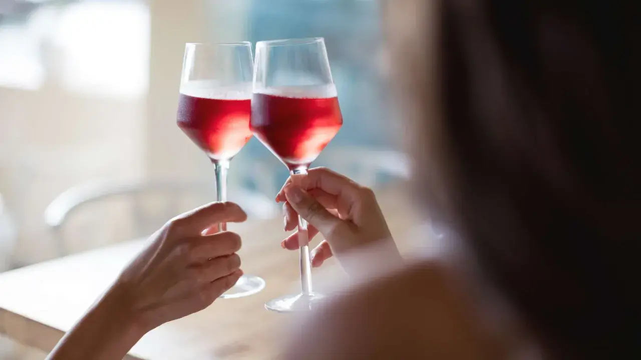 Dwie osoby wznoszą toast kieliszkami z różowym winem. Czy wino różowe powstaje z mieszania białego z czerwonym? Proces produkcji jest ciekawy!