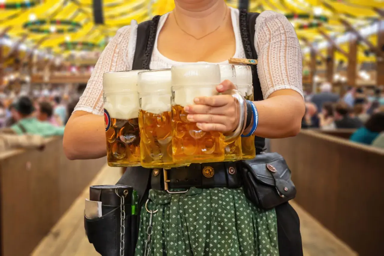 Kelnerka w tradycyjnym stroju niesie kufle piwa. Obrazek nawiązuje do tego, jakie są tradycje piwne w Czechach a jakie w Niemczech kultura picia.