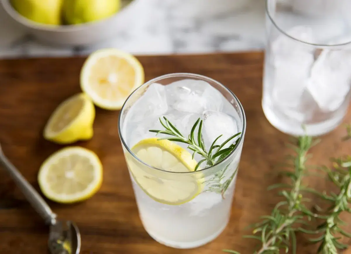 Orzeźwiający gin z tonikiem z plasterkiem cytryny i gałązką rozmarynu, otoczony świeżymi cytrynami.