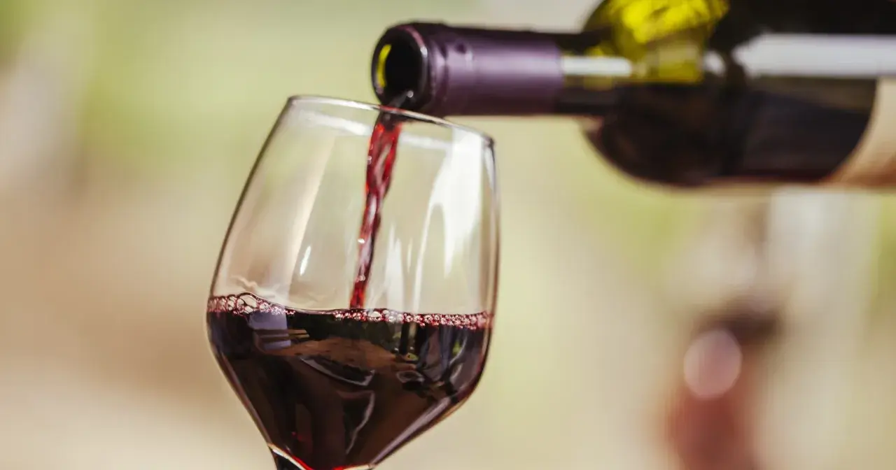 Czerwone wino nalewane do kieliszka. Widoczne "łzy" na ściance, świadczące o zawartości alkoholu.