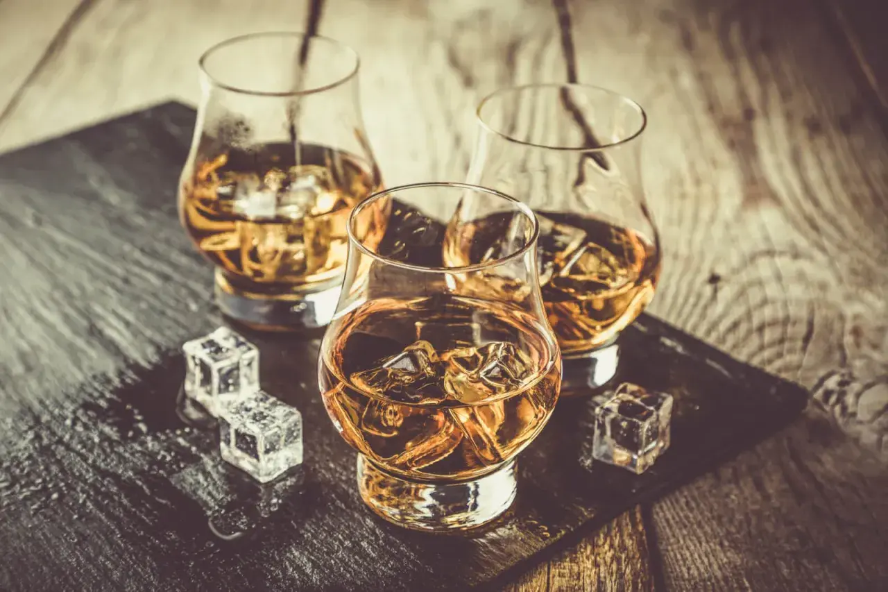 Trzy szklanki z bursztynową whisky i lodem na drewnianym blacie. Czy to sposób, jak poprawić smak whisky?