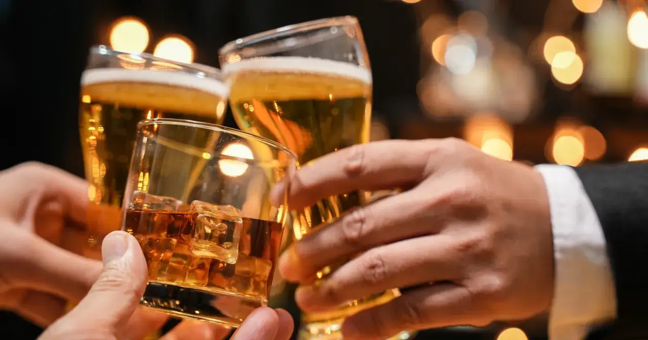 Trzy dłonie wznoszą kieliszki z piwem i whisky. Czy whisky jest zdrowe? To pytanie towarzyszy toastom.
