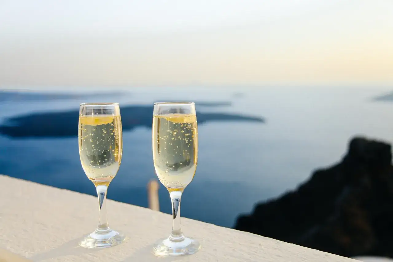 Dwa kieliszki musującego wina na tle morza. Zastanawiasz się, dlaczego wino musujące typu Prosecco jest tańsze od Szampana?