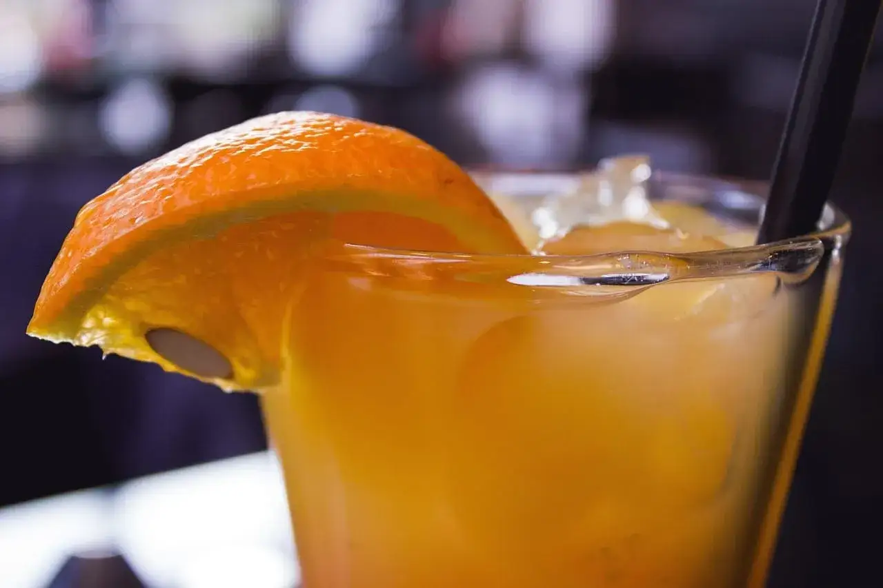 Orzeźwiający drink z pomarańczą, lodu i czarną słomką. Zest z cytrusów i zioła to najlepsze techniki garnirowania drinków.