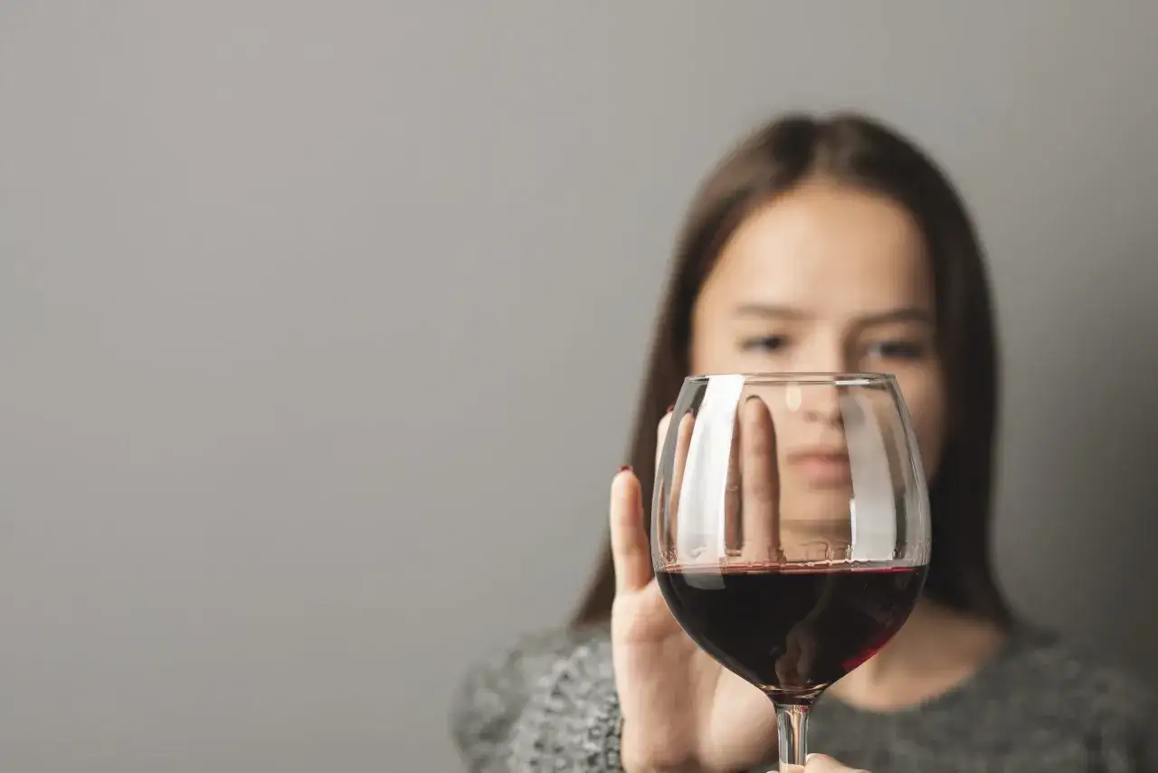 Kobieta odsuwa kieliszek z czerwonym winem, symbolizując świadomość objawów zatrucia alkoholem etylowym, pierwszej pomocy i środków ostrożności.