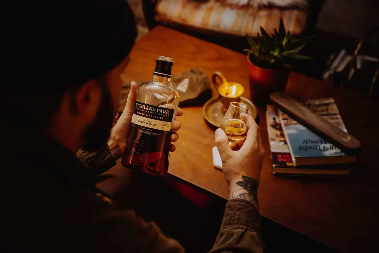 Jak sprawdzić czy stara butelka whisky z barku nadaje się do picia? Mężczyzna trzyma butelkę Highland Park i kieliszek, przy świecy.
