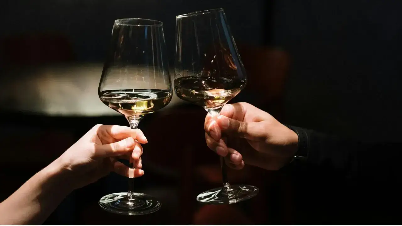 Dwie dłonie unoszą kieliszki z białym winem, ukazując subtelną różnicę między szczepem Chardonnay a Sauvignon Blanc w aromacie.