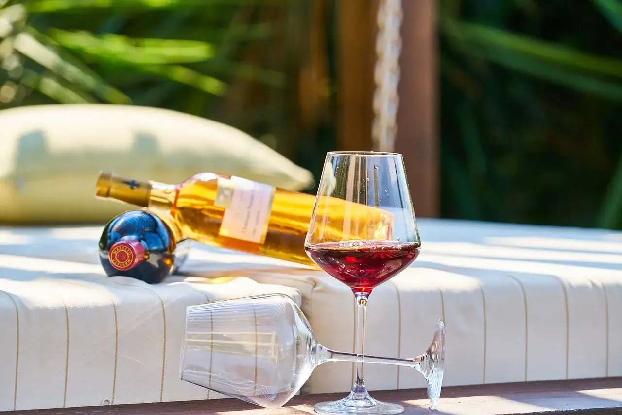 Skutki zbyt wysokiej temperatury serwowania: czerwone wino grzeje się, tracąc aromat. Kieliszek z winem i butelki na leżaku.