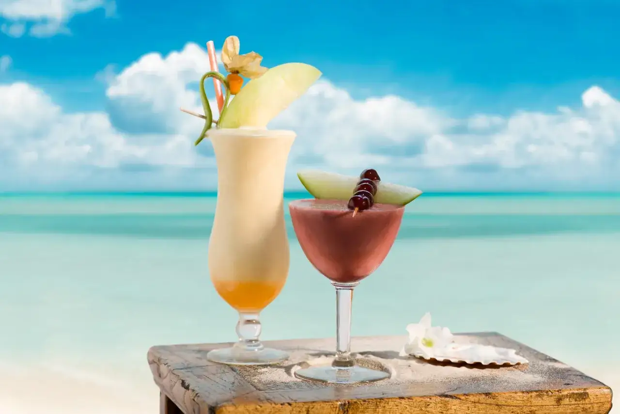 Dwa tropikalne drinki, jeden kremowy, drugi owocowy, z Malibu na plaży.