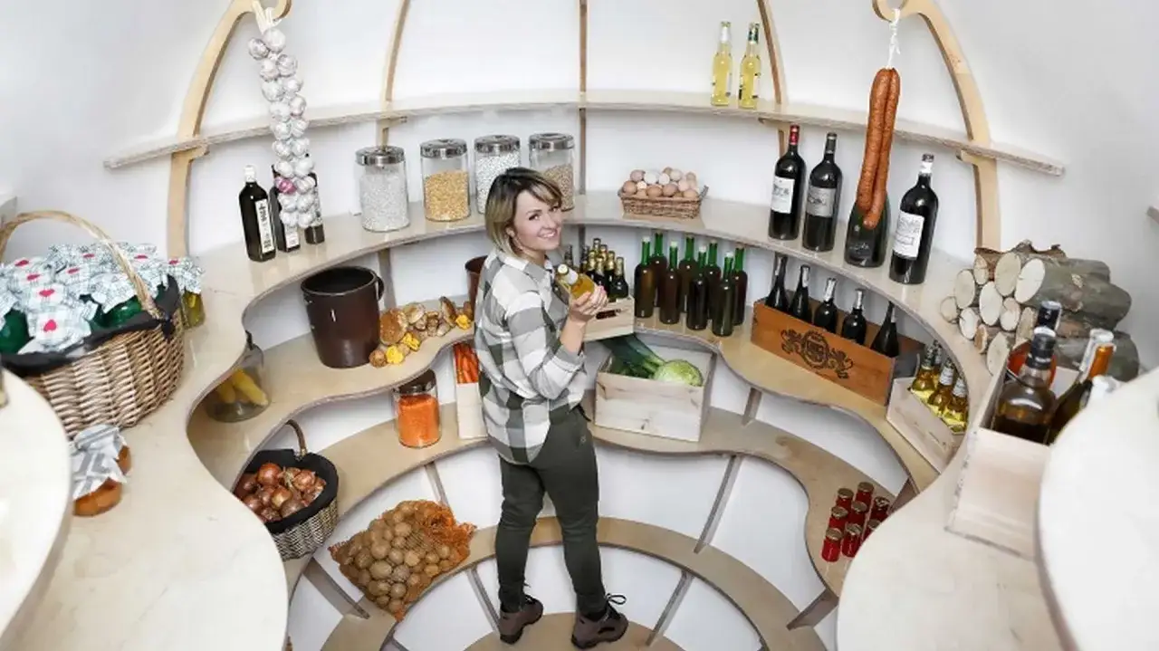 Kobieta w spiżarni z przetworami, warzywami i winem. Zastanawia się, czy wino się psuje, trzymając butelkę w dłoni.