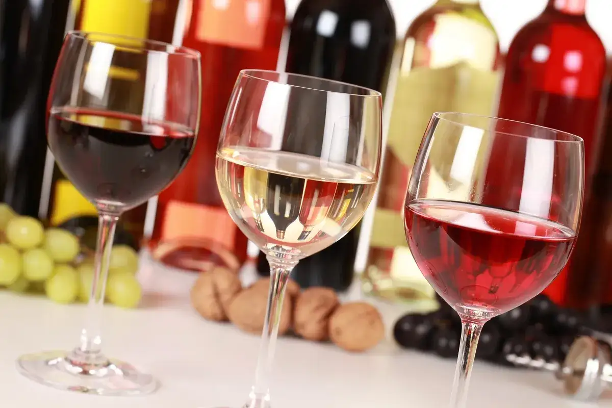 Trzy kieliszki z winem: czerwone, białe i różowe. W tle butelki i winogrona. Różnica między szczepem Chardonnay a Sauvignon Blanc w aromacie jest subtelna, ale wyczuwalna.