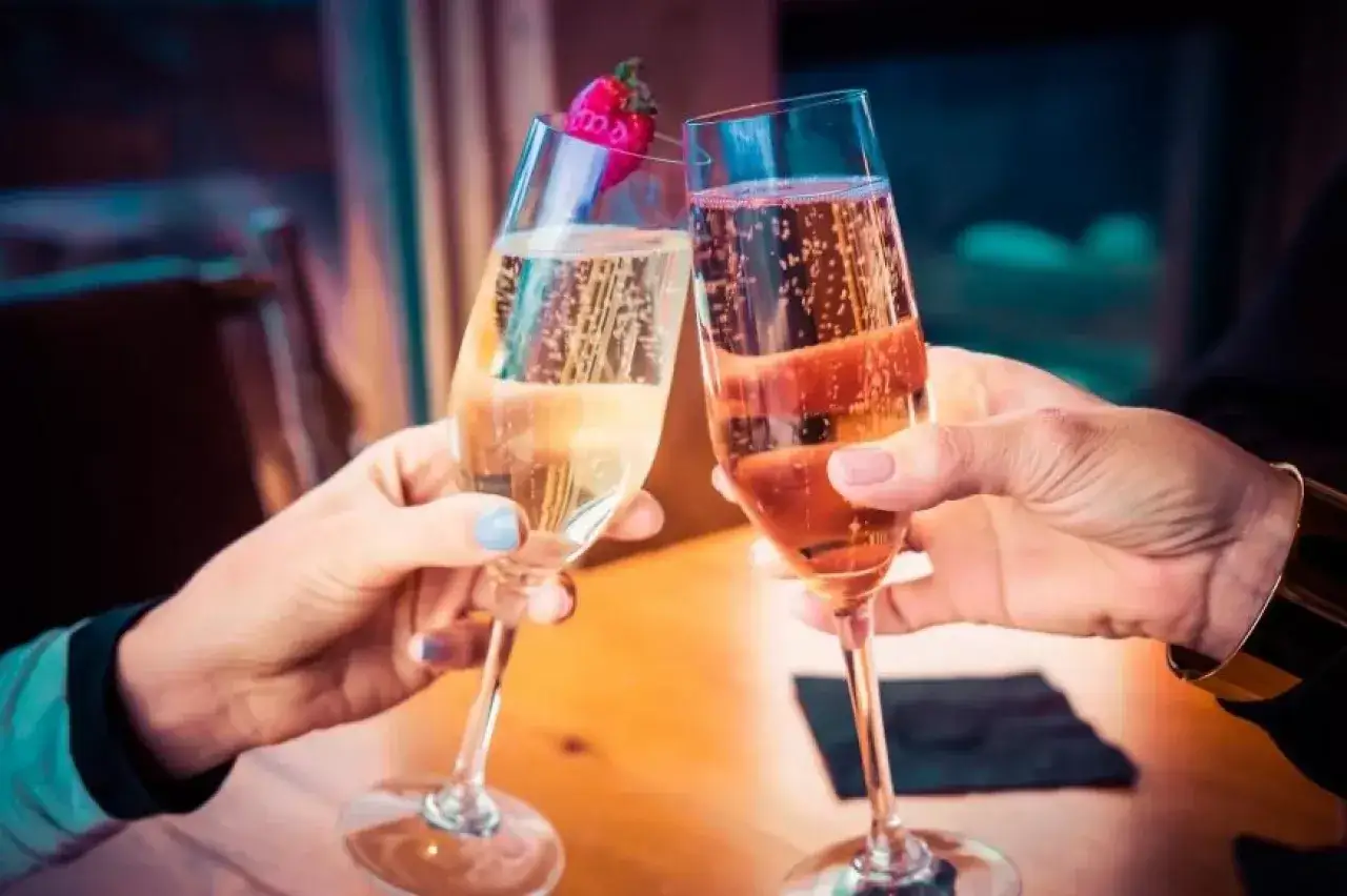 Dwie osoby wznoszą toast kieliszkami musującego wina. Zastanawiasz się, dlaczego wino musujące typu Prosecco jest tańsze od Szampana?