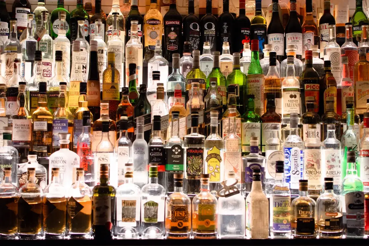 Rząd butelek alkoholi, od wódki po piwo, w barze. Co lepiej pić wódkę czy piwo?