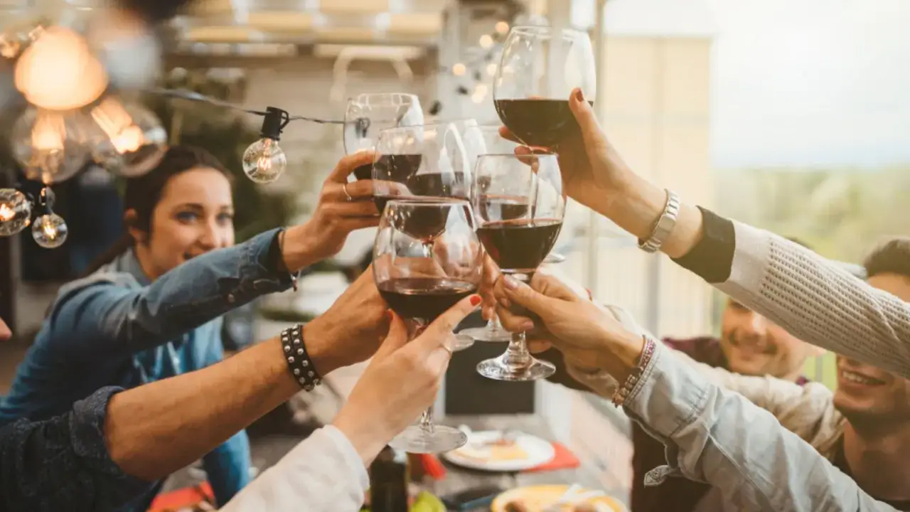 Przyczyny bólu głowy po winie: siarczyny czy taniny? Grupa przyjaciół wznosi toast czerwonym winem, zastanawiając się, co bardziej szkodzi.