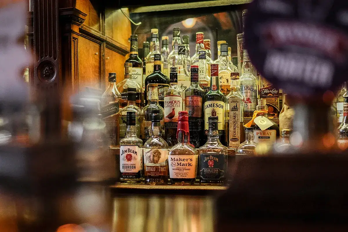Butelki whisky na półce. Metaliczny posmak i pieczenie to objawy niskiej jakości whisky zbożowej.