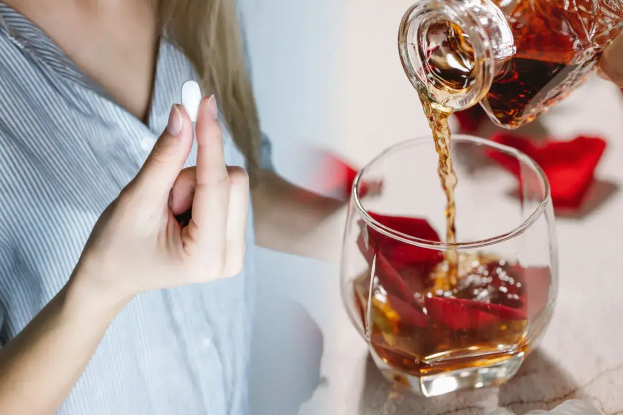 Kobieta trzyma tabletkę, zastanawiając się, czy po whisky jest kac. Bursztynowy trunek leje się do kieliszka.