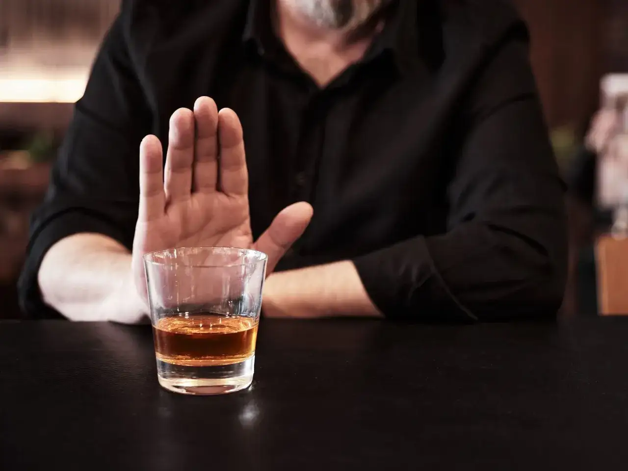 Mężczyzna odrzuca kieliszek whisky, sugerując, że nie wierzy, iż whisky jest zdrowe.