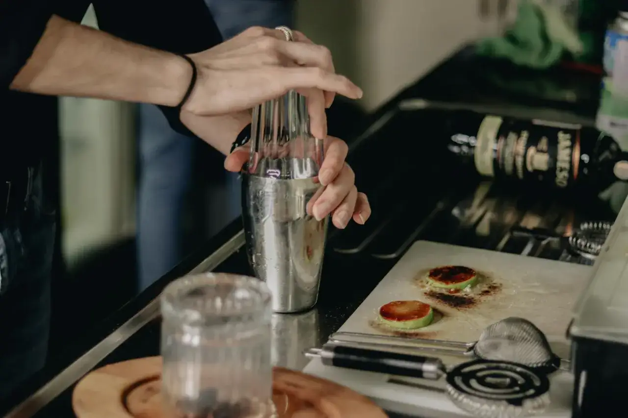 Skutki przegrzania składników podczas muddlowania: przypalone plasterki jabłka na desce, obok shaker i butelka whisky.