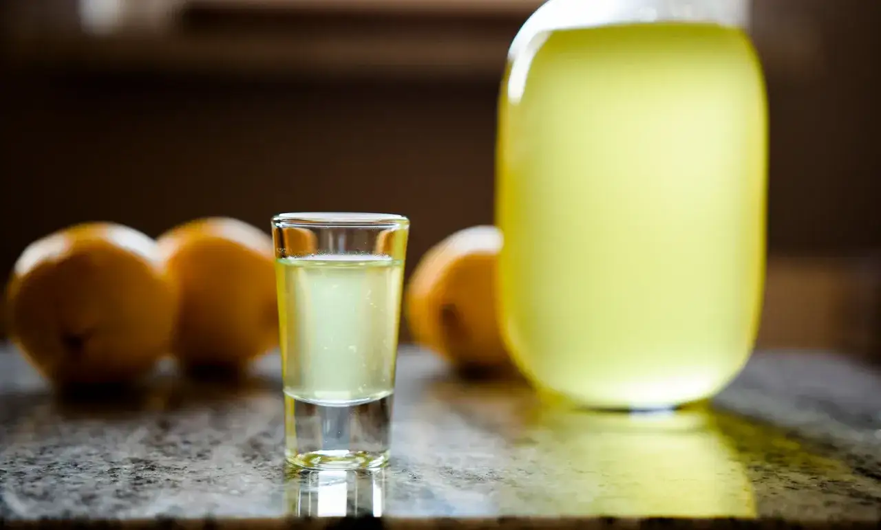 Szklaneczka orzeźwiającego drinka z limoncello, obok cytryny i dużej butelki tego włoskiego likieru.