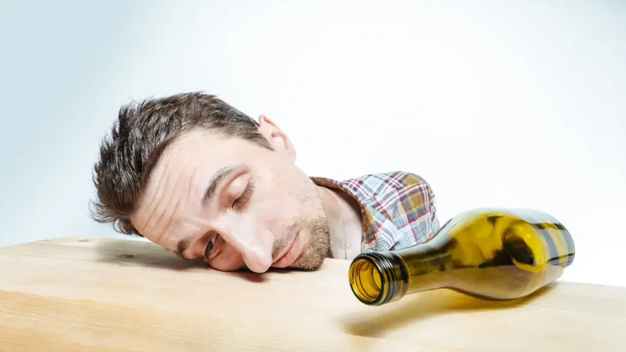 Mężczyzna śpi na stole obok pustej butelki. Objawy zatrucia alkoholem etylowym, pierwsza pomoc i środki ostrożności.