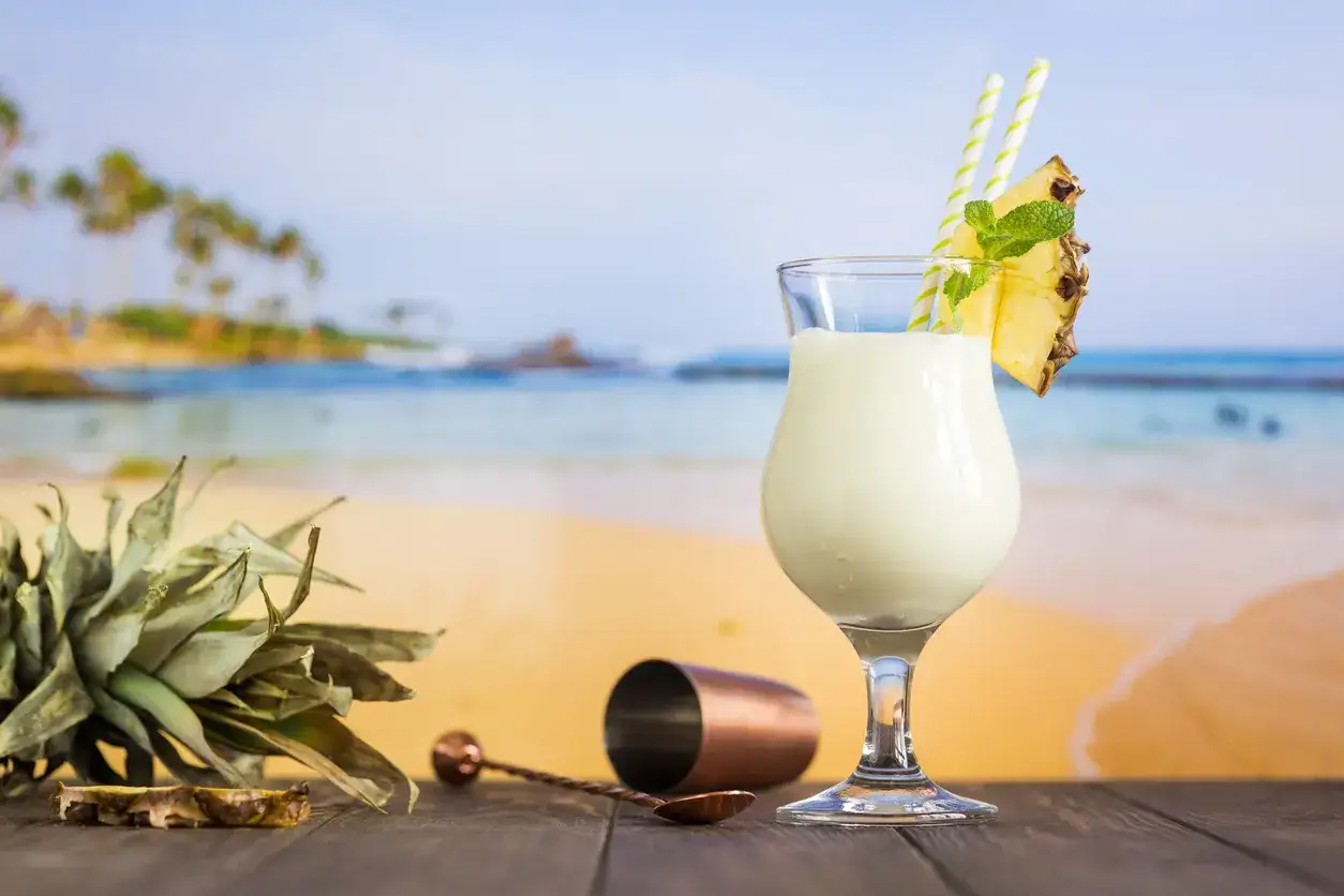 Orzeźwiający drink pina colada na tropikalnej plaży. Obok ananas i akcesoria barmańskie.