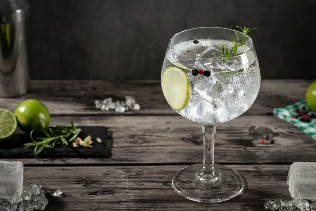 Orzeźwiający gin z tonikiem, udekorowany plasterkiem limonki, rozmarynem i pieprzem, na drewnianym blacie.