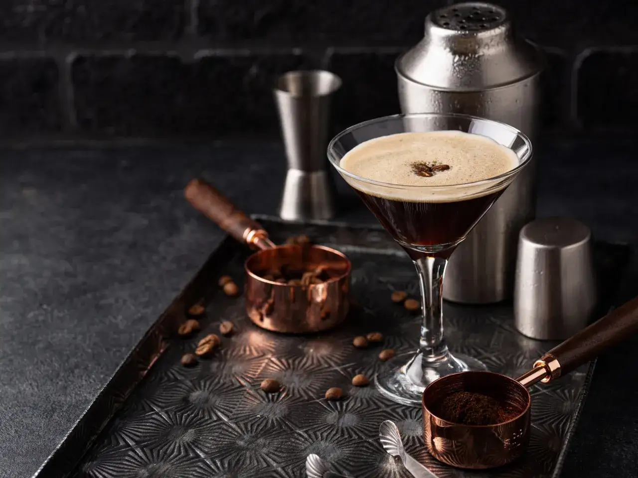 Espresso Martini z gęstą cremą, przygotowane z kawy i ziaren. Obok shaker i miarki.
