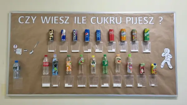Tablica edukacyjna pokazuje, ile cukru jest w popularnych napojach. Obok każdej butelki i puszki znajduje się woreczek z odpowiadającą ilością kostek cukru.